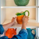 A Woman Putting a Orange Jar on a Shelf Copy