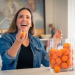 A Smiling Woman Picking a Tangerine from a Jar One